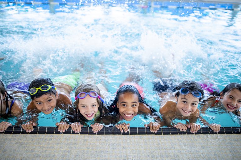 A group of elementary school children are at the pool. They are smiling and posing for the camera.