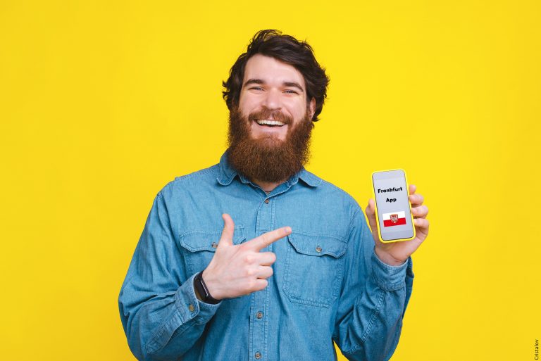 Porträt eines fröhlichen jungen Mannes mit Bart, der auf Smartphone-Bildschirm über gelbem Hintergrund zeigt
