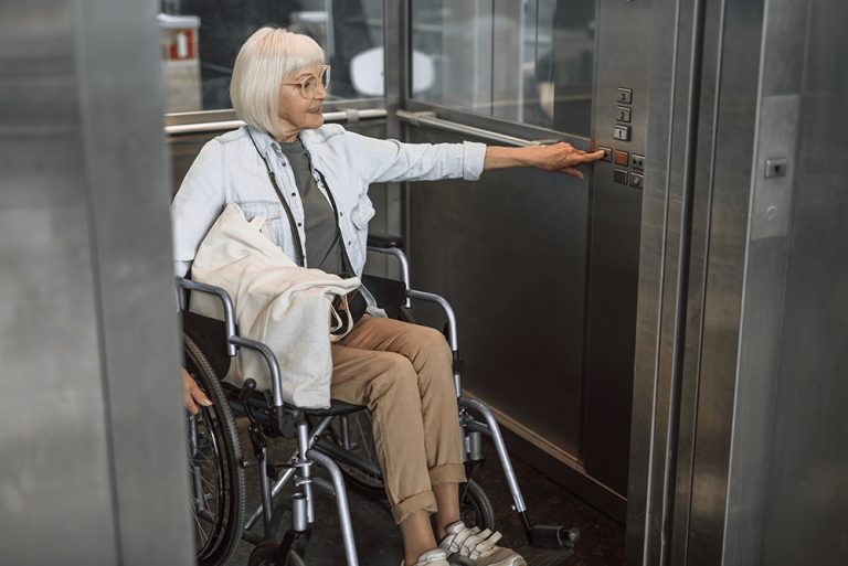 Reife Frau in Brille auf Rollstuhl mit Aufzug
