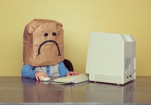 Junge mit Tüte über dem Kopf mit traurigem Gesicht vor einem Computer