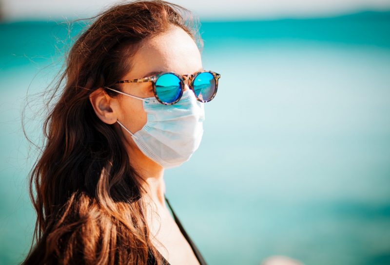 Frau trägt schützende Gesichtsmaske am Strand