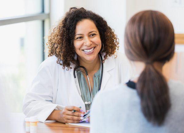 A smiling mid adult female doctor listens as a female patient discusses her health.